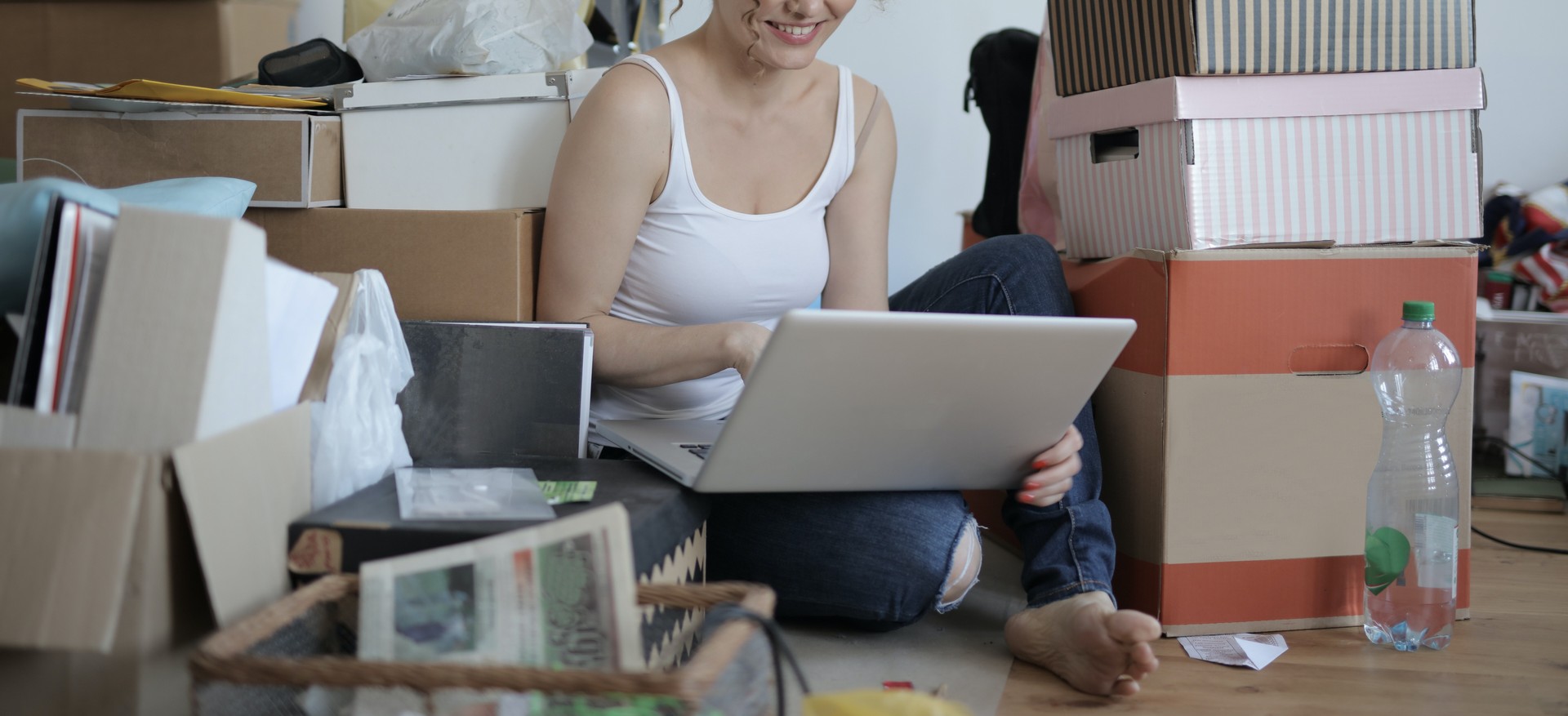 smiling girl sitting on floor with boxes and looking into a laptop